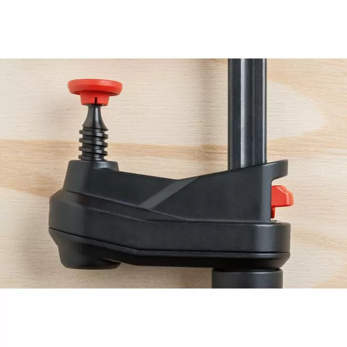 Close-up of woodworking clamp with black body and red adjustment knobs on wood surface