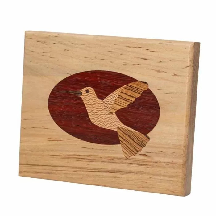 Woodworking inlay of a hummingbird in light and dark wood with an oval background.
