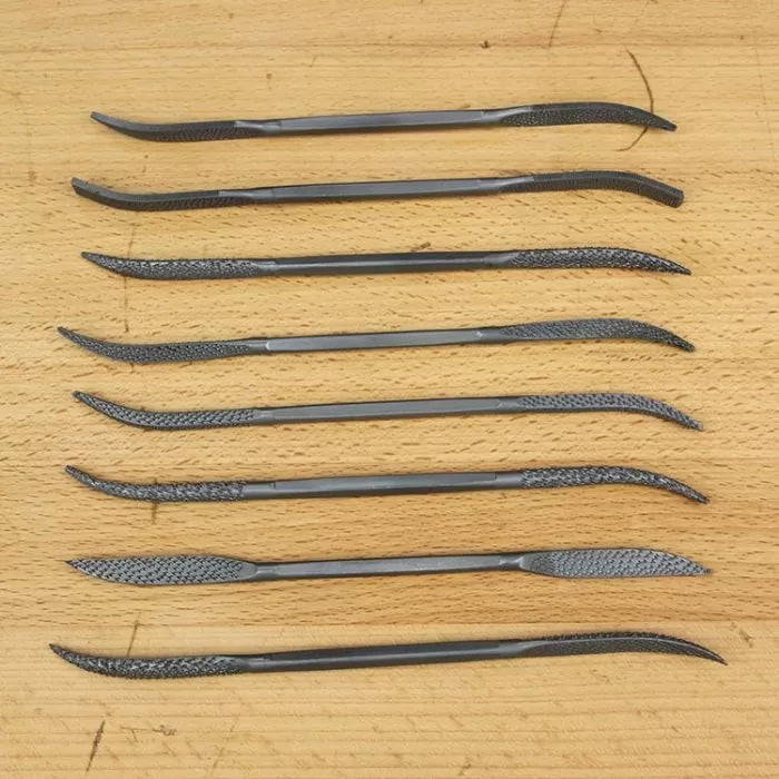 Set of eight curved woodworking rasps on a wooden surface for wood carving and detailing