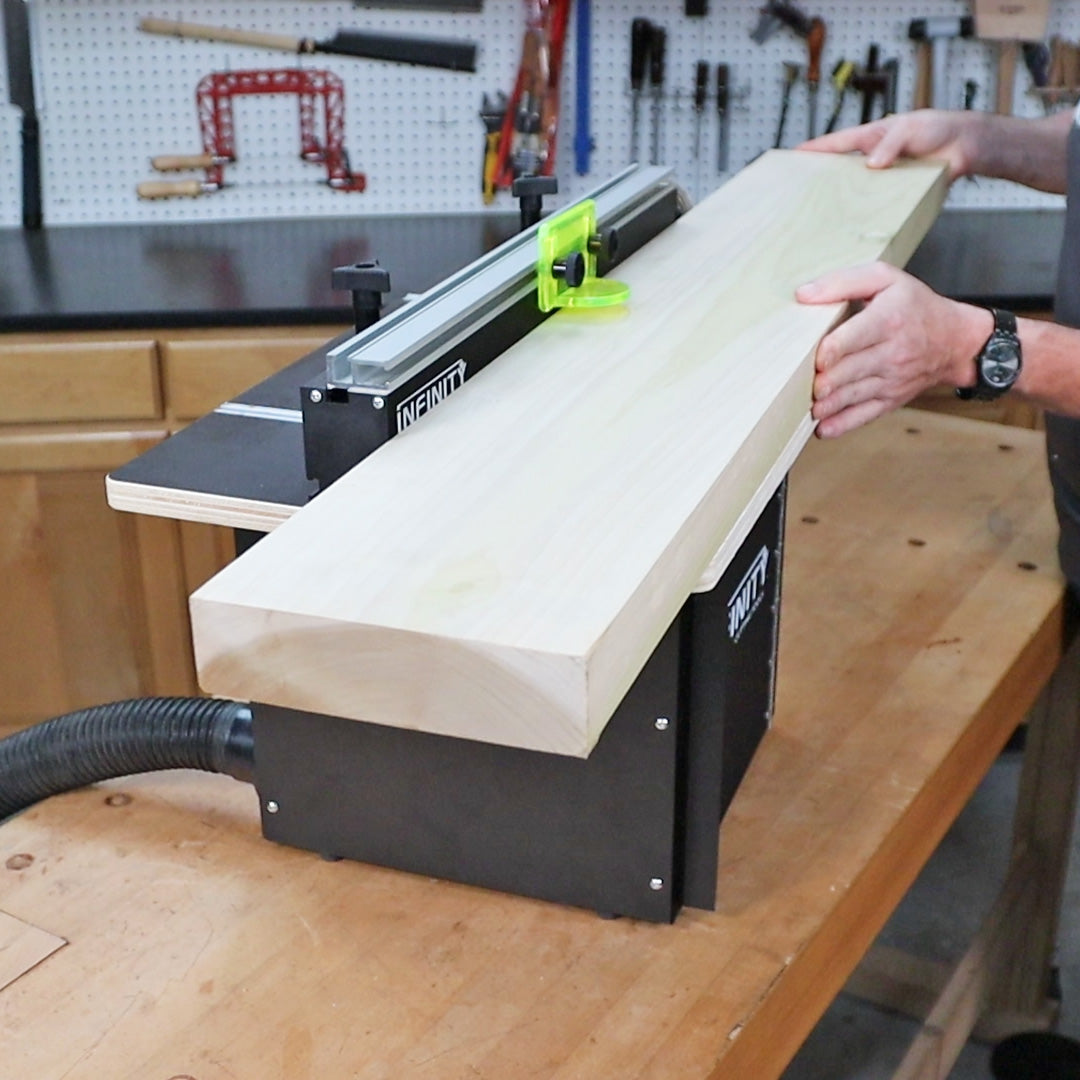 Woodworker using a router table to shape an edge on a large wood board in a workshop.