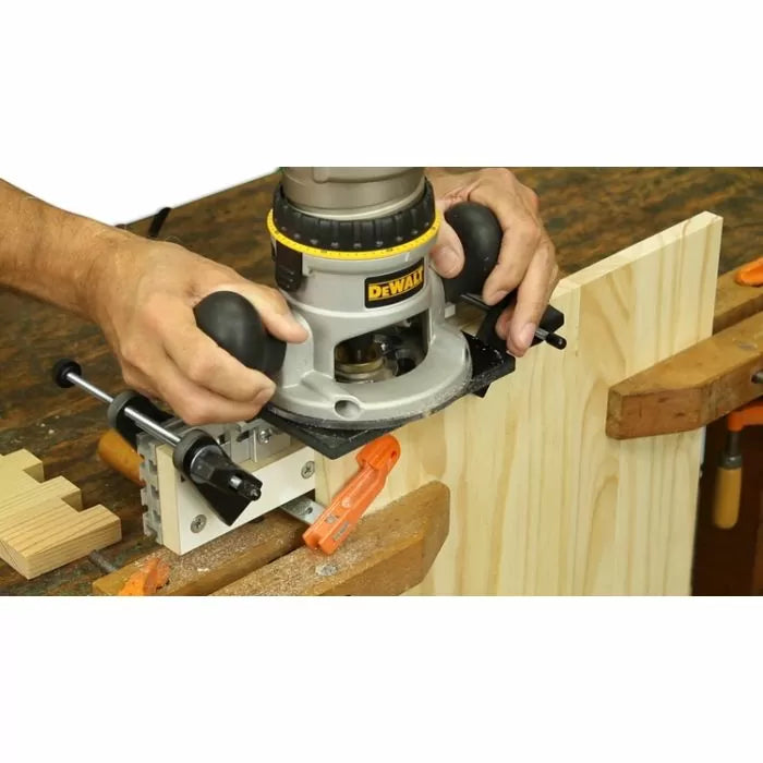 Woodworker using a handheld router and dovetail jig to cut joinery in a wooden board