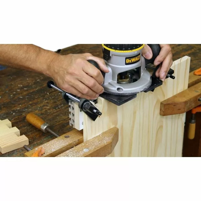 Woodworker using a router and dovetail jig to cut joinery in a wood board on a workbench