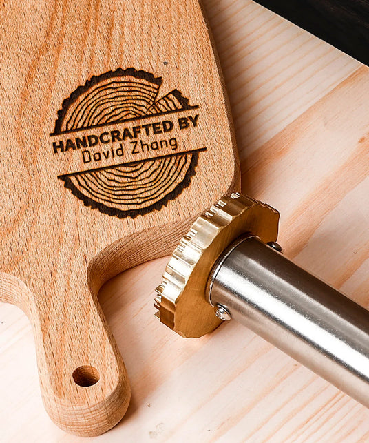 Custom branding iron next to engraved wooden cutting board on light wood surface