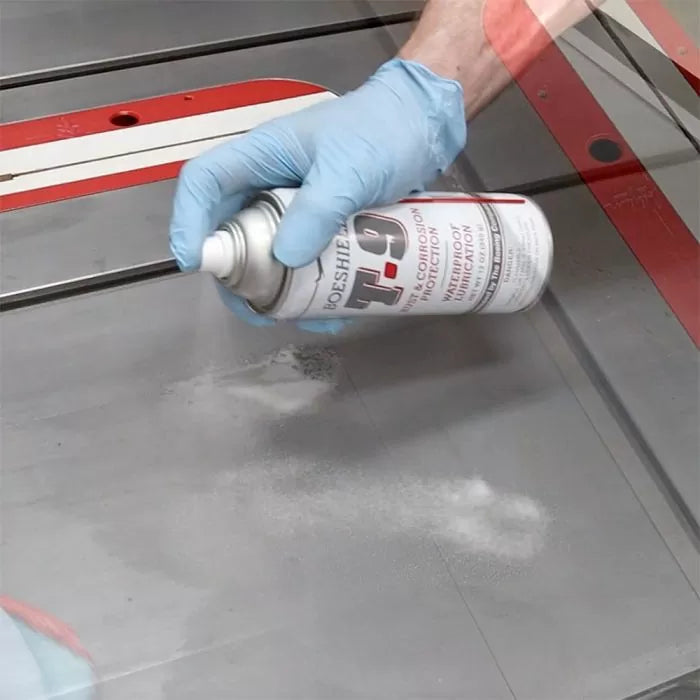 Gloved hand spraying T-9 lubricant on a table saw surface for rust prevention and tool maintenance.