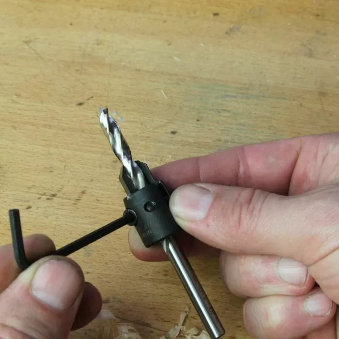 Person adjusting woodworking drill bit with hex key on a wooden workbench