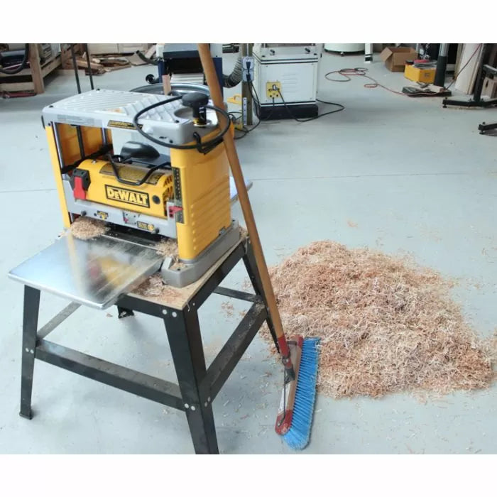 Benchtop wood planer on stand with shavings and broom in woodworking shop
