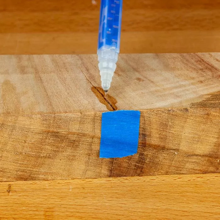 Applying wood glue to a crack in a wooden board with blue painter's tape for woodworking repair