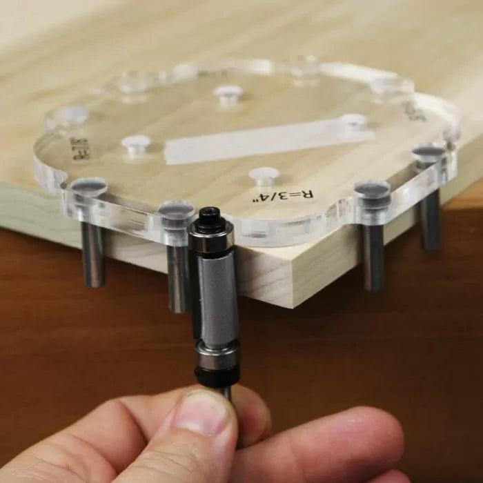 Clear router template with guide pins on wood edge, hand holding router bit, woodworking tool