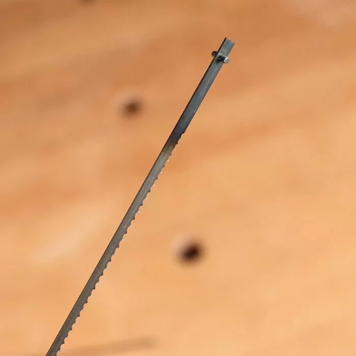 Close-up of a scroll saw blade with fine teeth for woodworking on a wooden background.
