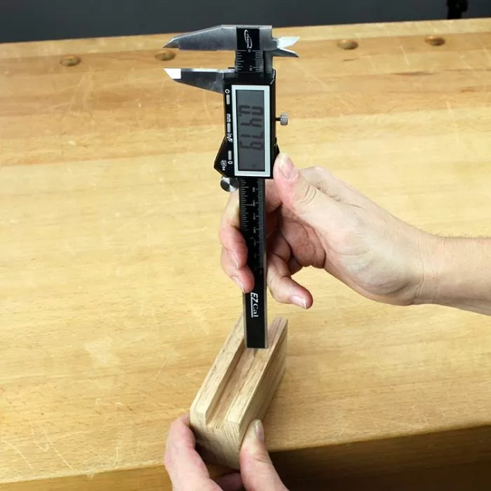 Digital caliper measuring wooden block thickness on woodworking bench