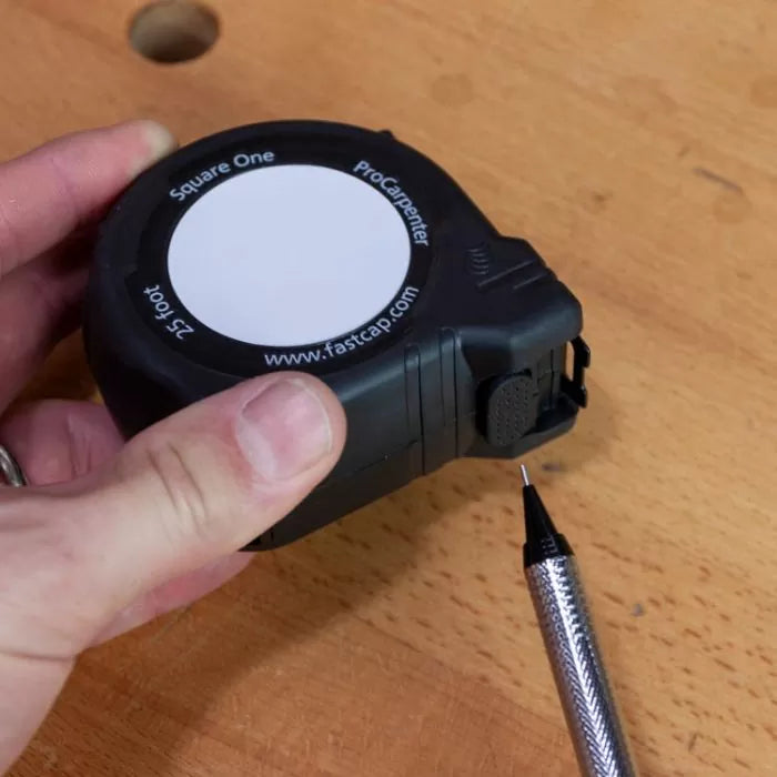 Hand holding a ProCarpenter tape measure with pencil on a wood workbench.