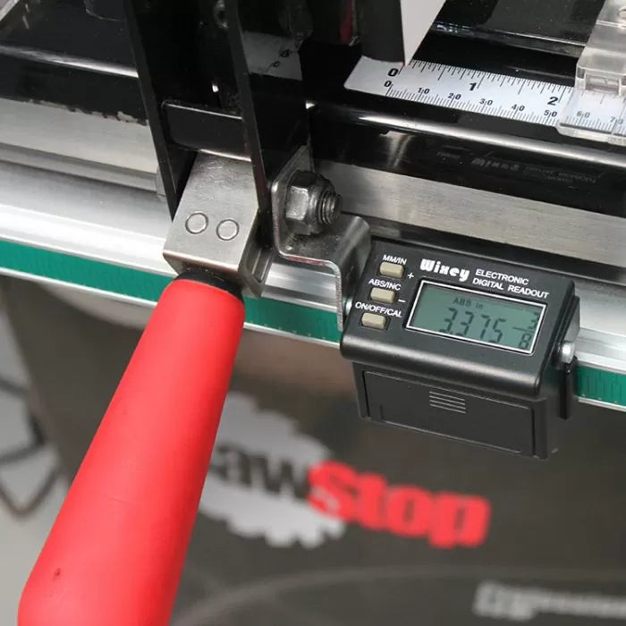 Close-up of digital readout gauge attached to table saw fence with red handle for precise measurements