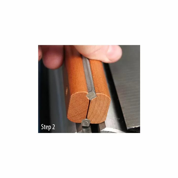 Hand holding wooden jig with V-groove guiding a steel rod on a table saw, step 2
