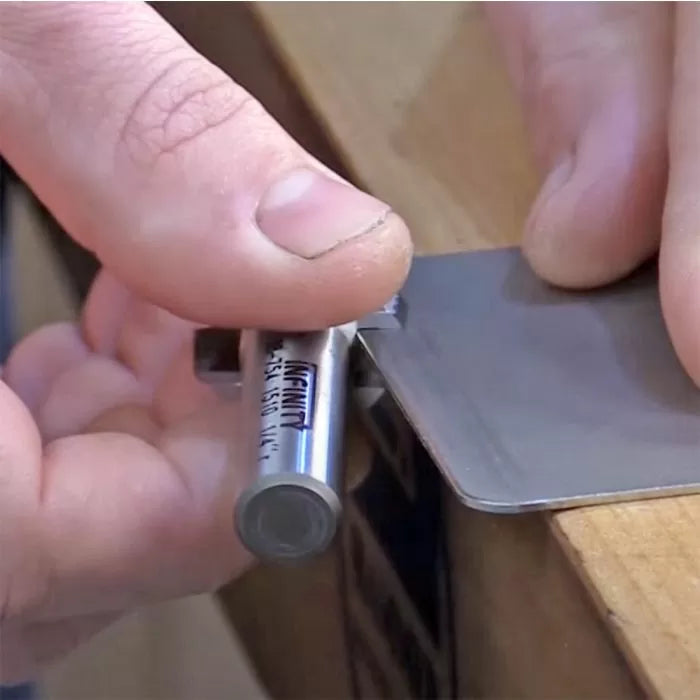 Hand using a burnisher tool to sharpen a cabinet scraper on a workbench