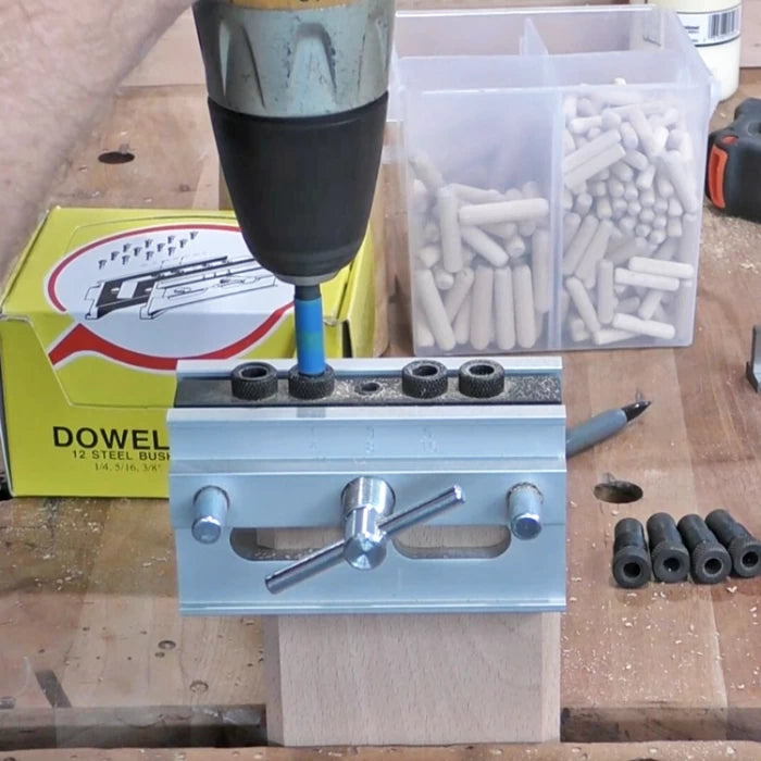 Woodworker using a dowel jig and drill on a wooden board with dowel pins nearby