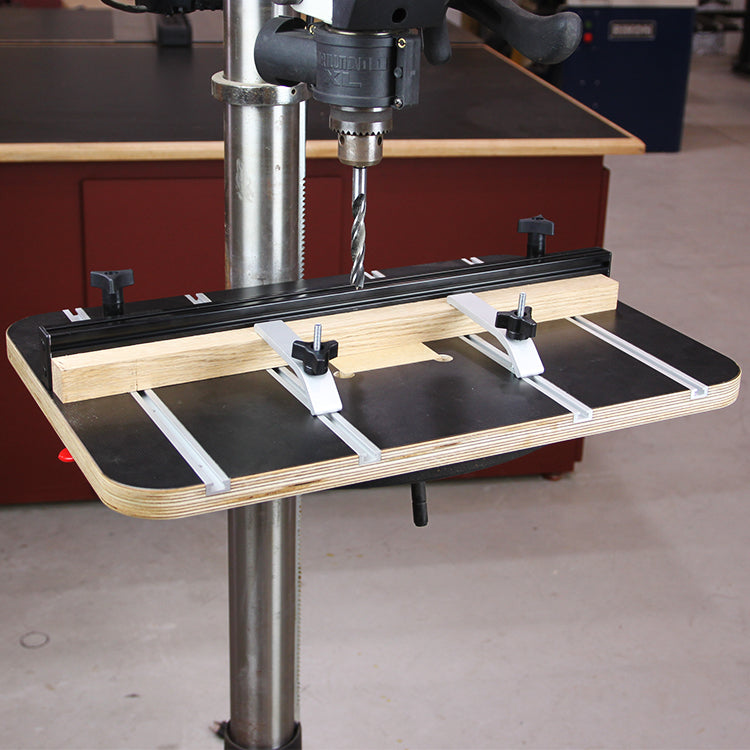 Drill press table with adjustable fence and hold-down clamps in a woodworking shop