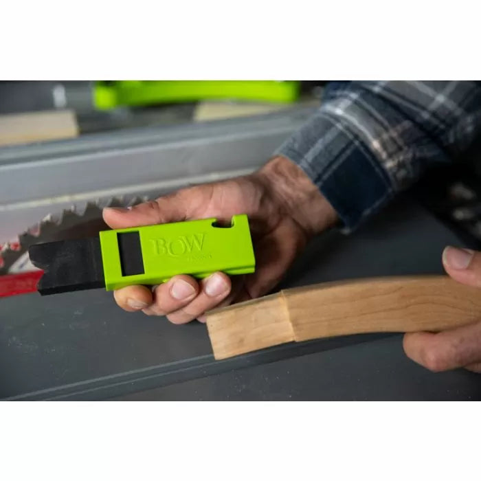 Person holding a green woodworking featherboard tool near a saw blade and curved wood piece