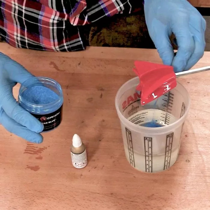 Mixing blue resin pigment into clear epoxy with a stirrer on a woodworking table