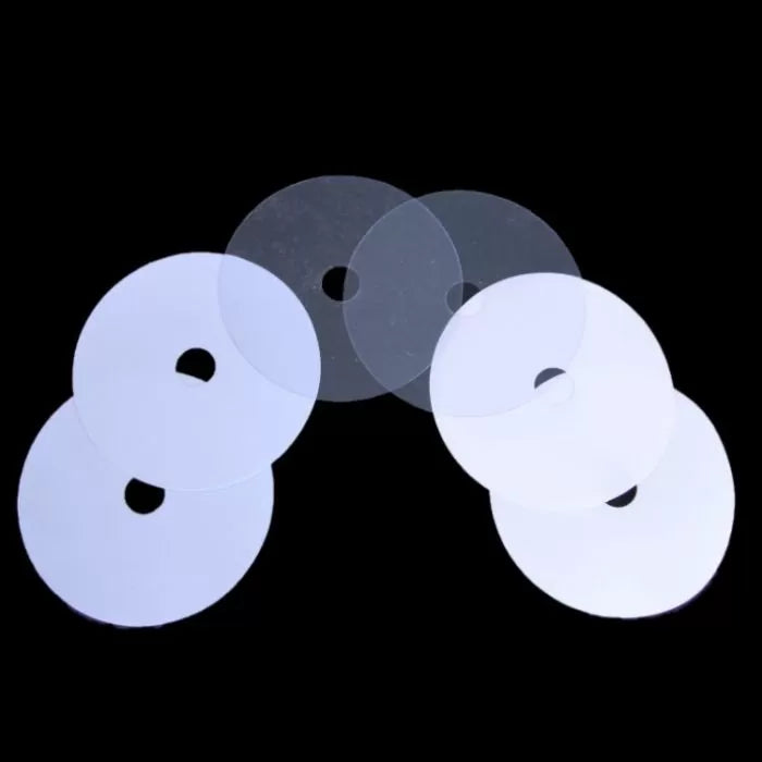Set of six clear plastic shims for woodworking tools, round with center holes, on black background.