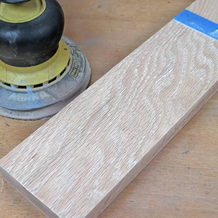 Electric sander with sanded hardwood board on a woodworking bench