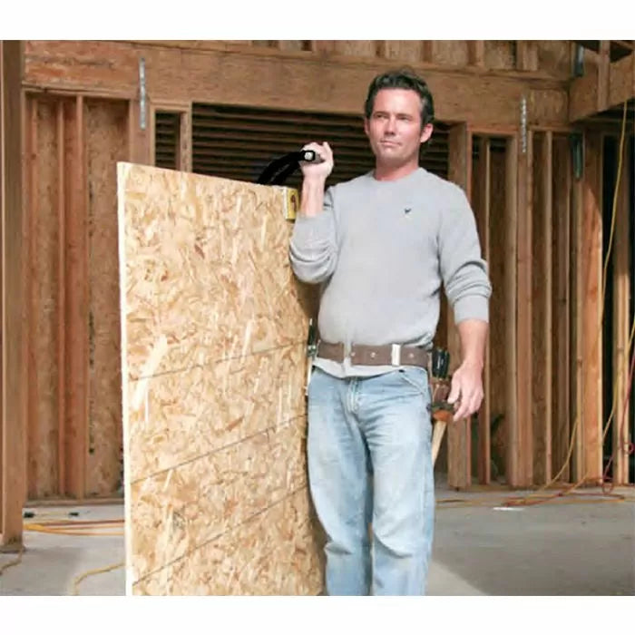 Man using a panel gripper tool to carry a large sheet of plywood at a construction site
