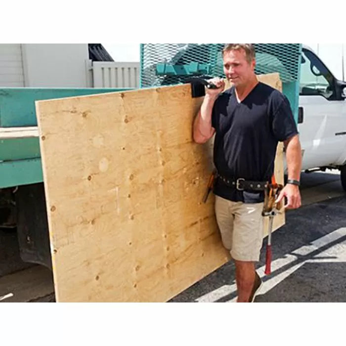 Man using a gripper tool to carry a large sheet of plywood at a construction site