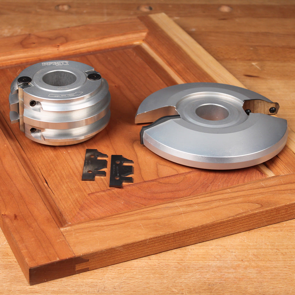 Cabinet door shaper cutters and carbide inserts on a wooden panel in a woodworking shop