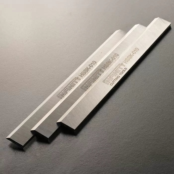 Set of three high-speed steel planer blades for woodworking tools on a dark background.