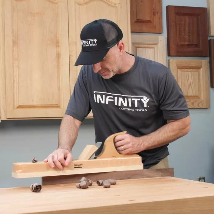 Woodworker using a hand plane on a workbench, wearing a mesh cap in a workshop