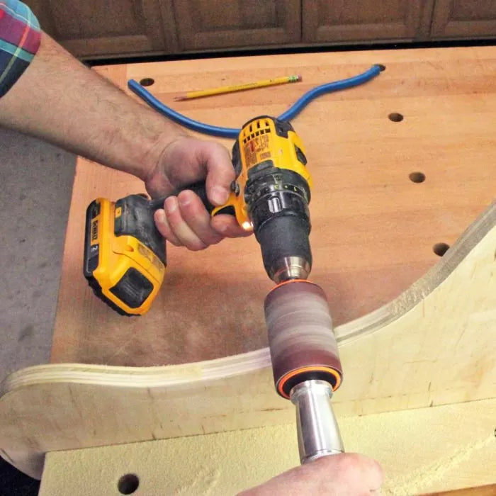 Cordless drill with sanding drum smoothing curved wood edge on workbench