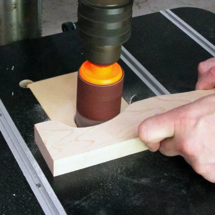Oscillating spindle sander shaping a wooden board in a woodworking workshop.
