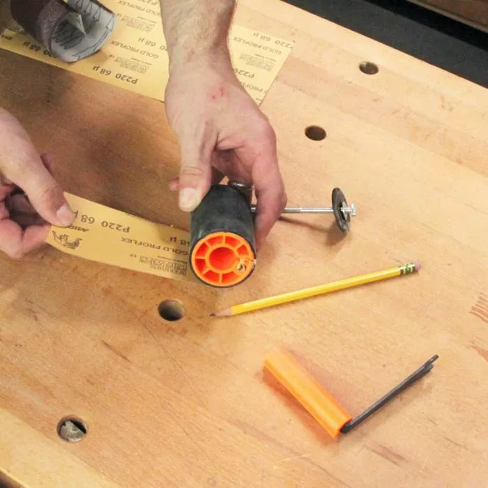 Hand assembling sanding drum with sandpaper on woodworking bench with pencil and tools visible