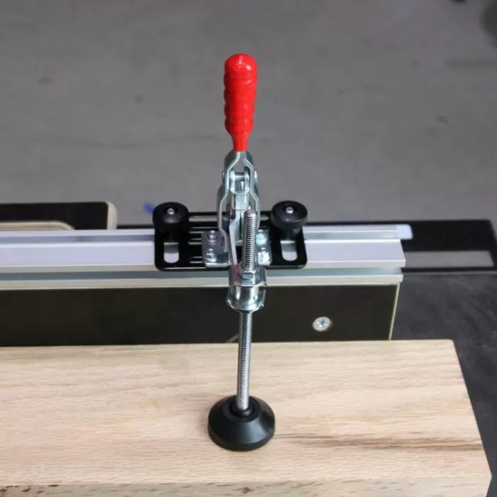 Toggle clamp with red handle securing wood on a router table fence in woodworking shop