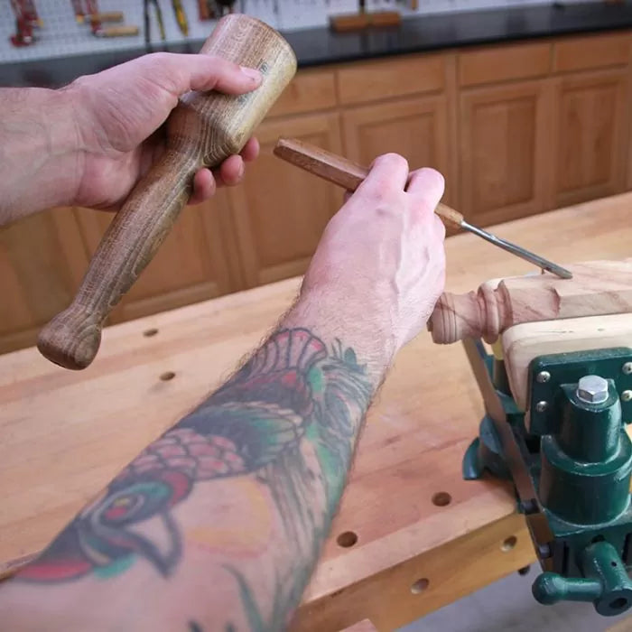 Woodworker using a chisel and mallet to carve wood on a workbench in a workshop