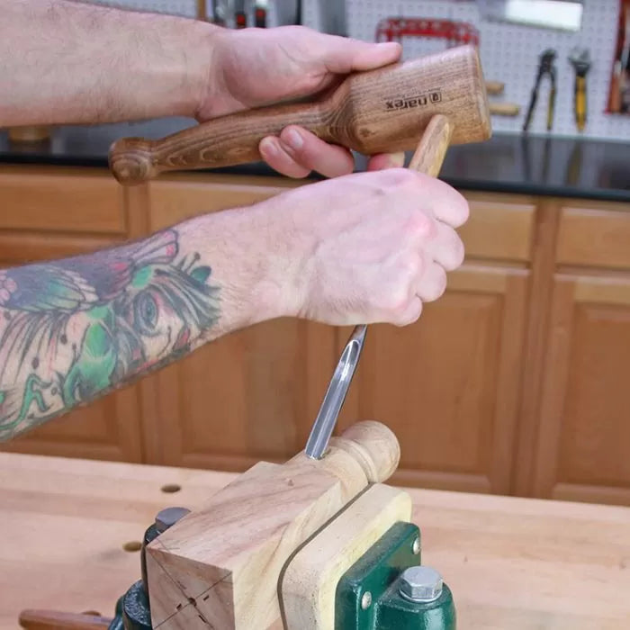 Woodworker using mallet and chisel to carve wood block secured in vise