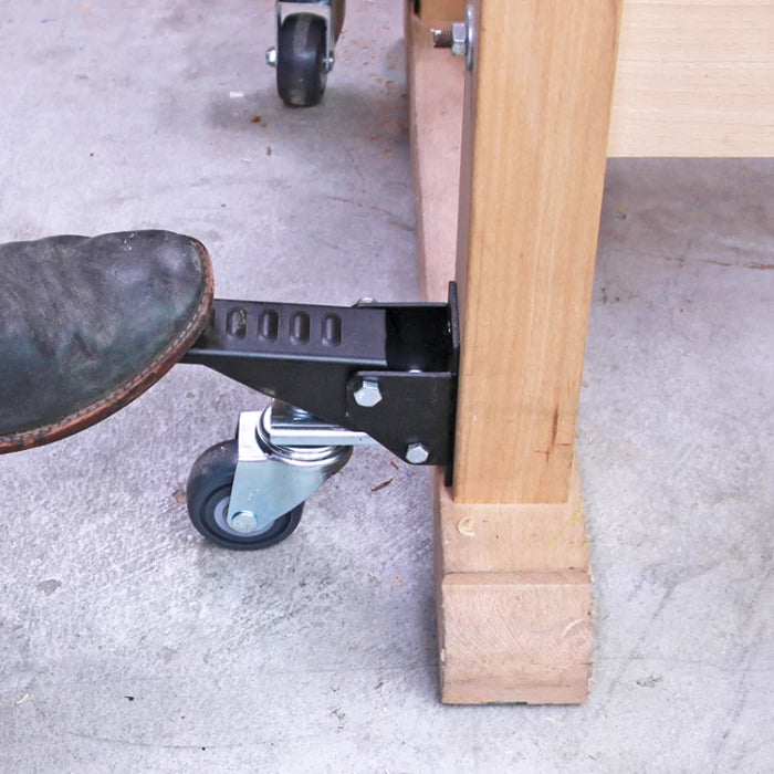 Woodworker using foot to activate adjustable workbench caster wheel on wooden table