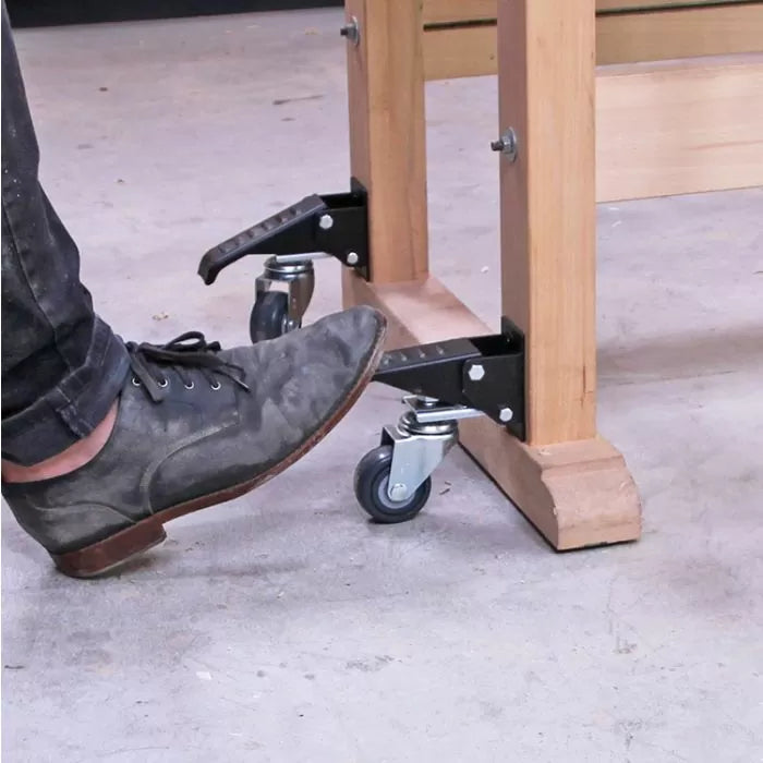Person using foot pedal to lift workbench on caster wheels in woodworking shop