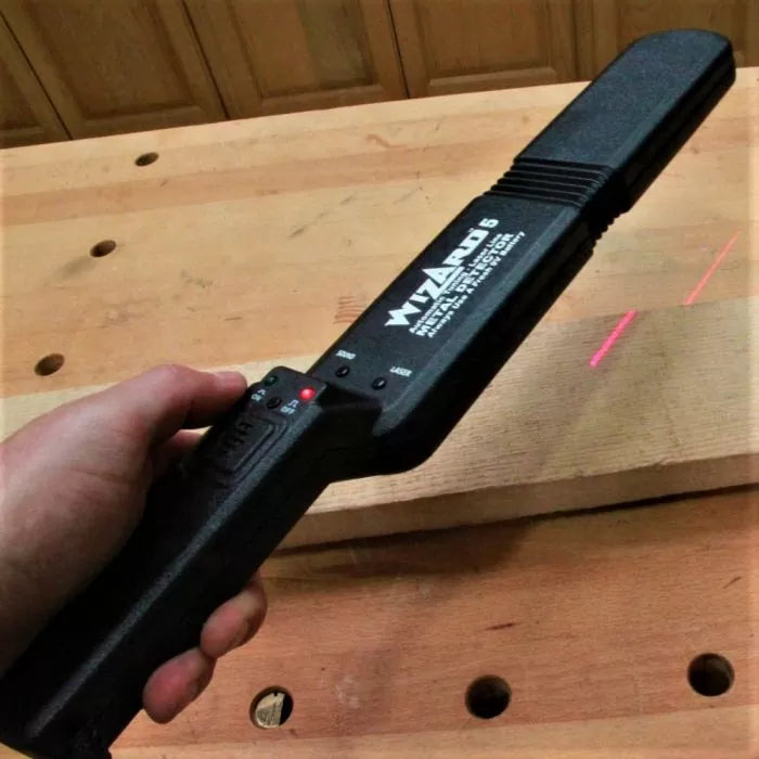 Handheld metal detector scanning a wooden board on a workbench in a woodworking shop