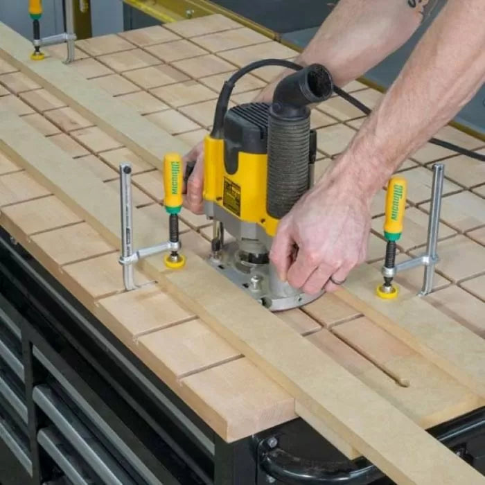 Woodworker using a router with jig system to cut precise grooves in a wood workbench top.