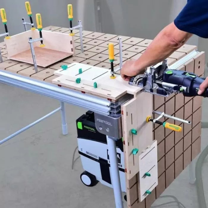 Woodworking jig system in use with clamps and power tool on a perforated workbench