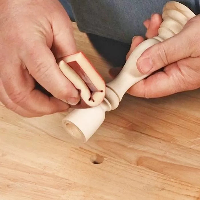 Hand sanding a turned wood spindle with a detail sanding block on a woodworking bench.