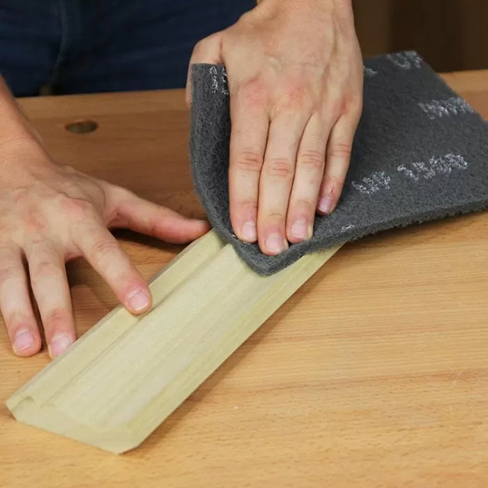 Hand sanding a wood molding with abrasive pad on workbench for woodworking finishing