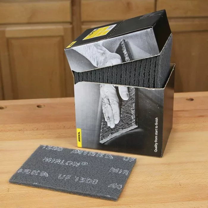 Box of grey non-woven abrasive pads on a wooden workbench, one pad displayed in front