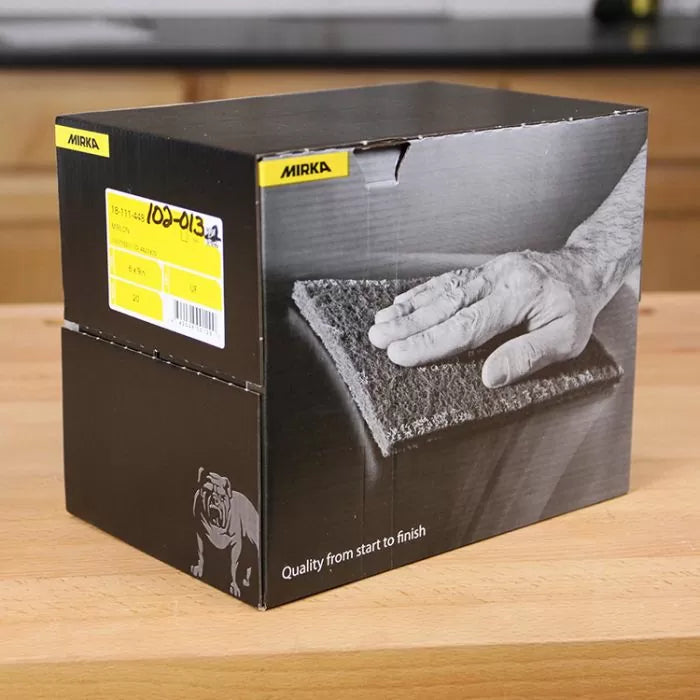 Mirka abrasive hand pads box on wooden workbench, ideal for woodworking and surface finishing.