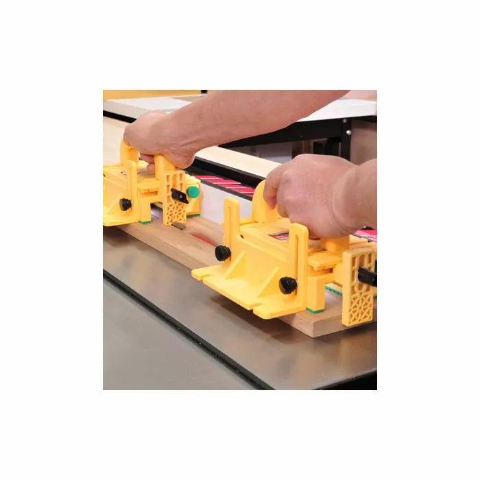 Hands using yellow push blocks for safe woodworking on a table saw with wood board