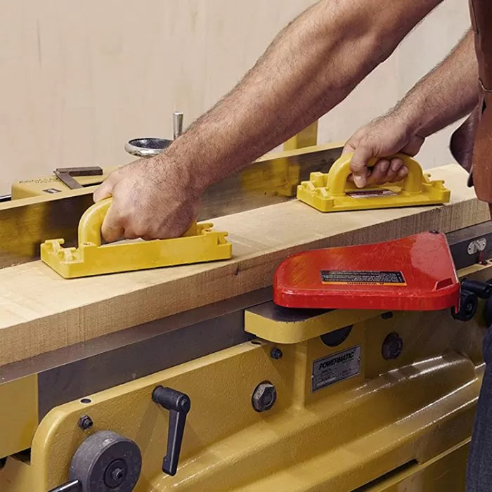 Woodworker using yellow push blocks on a jointer to smooth a wooden board
