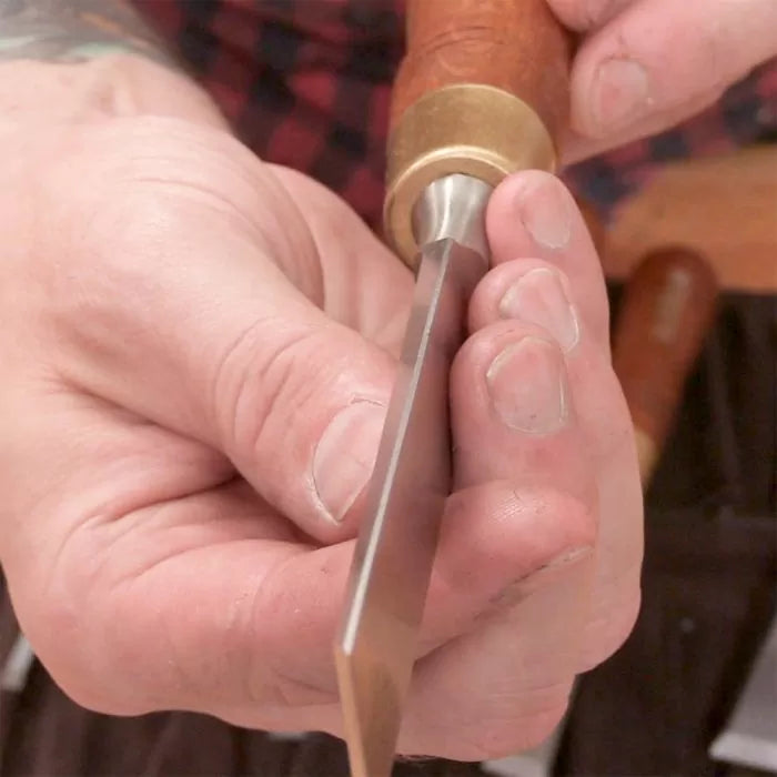 Close-up of hands holding a woodworking chisel with sharp beveled edge and wooden handle