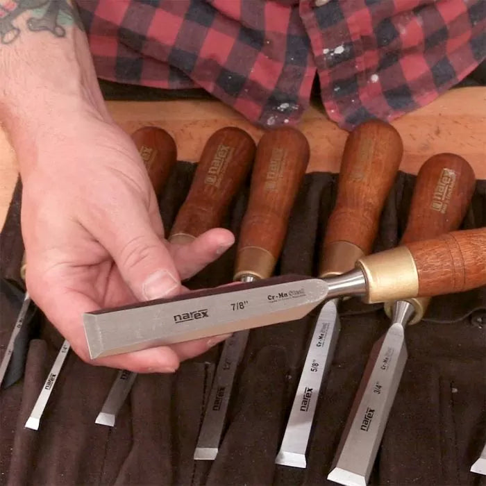 Hand holding woodworking chisel with wood handle, chisel set displayed in tool roll