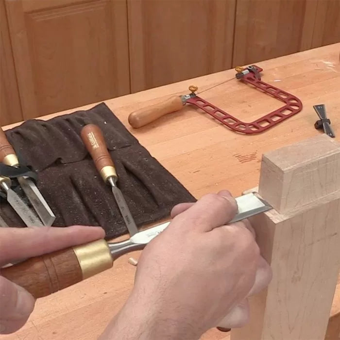 Woodworker using a chisel to refine a mortise and tenon joint on a workbench