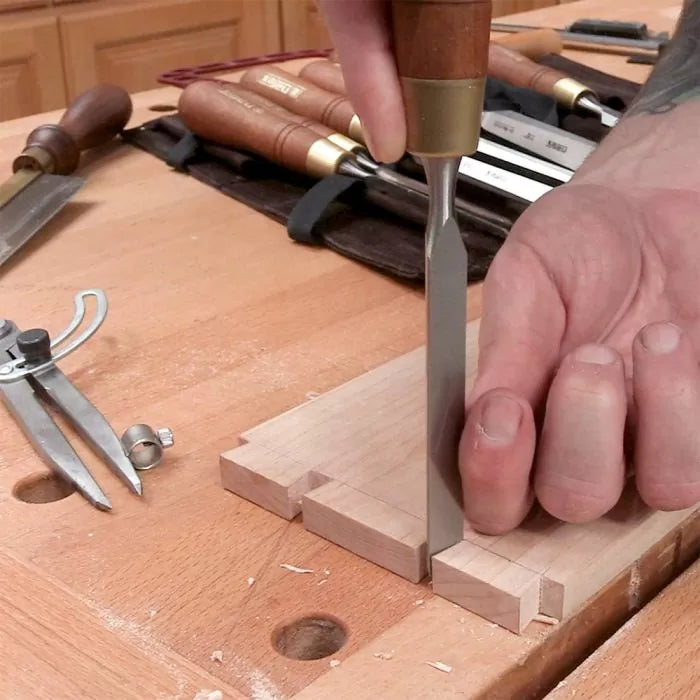 Woodworker using chisel to cut dovetail joint on hardwood at a woodworking bench